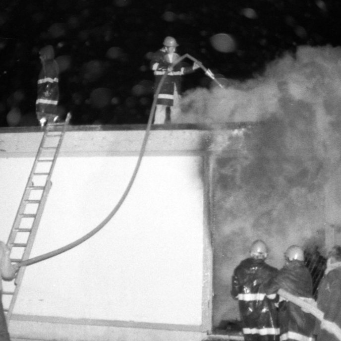 Spennistöðin brennur. Slökkviliðinu tókst að ráða niðurlögum eldsins, en miklar skemmdir urðu á spennistöðinni, Þarna eru slökkviliðsmennirnir að berjast við eldinn, bæði ofan af þakinu og inn í húsið í gegnum dyrnar.