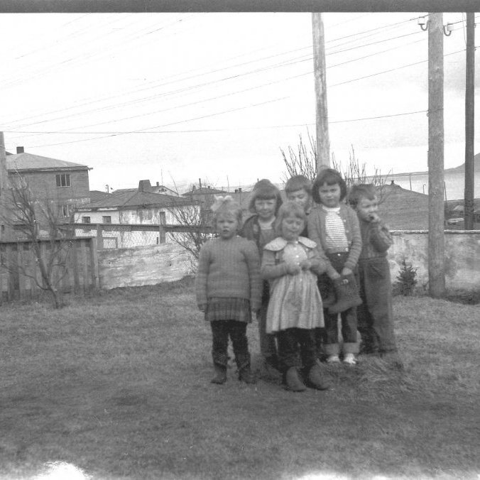Börn við Grundargötu 19 á lóðinni hjá Bæring. Lengst til vinstri er Erna Eyjólfsdóttir,  Ágústa Hinriksdóttir?, Ásdís Hinriksdóttir, Guðlaugur Pálsson, Sigríður Gísladóttir og Magnús Gíslason. Á móti er Húsið númer 20 fokhelt, síðan er það hús númer 24 Björgvinshús en þar bjó Björgvin Bjarnason. Svo er það blokkin, verið er að vinna við þakið á húsi númer 28 sem er langt komið og síðan er greinilega flutt inn á efstu hæðina á númer 26 en þar bjuggu Jón og Munda og börn þeirra og síðan á miðhæðinni Sigurjón og Guðveig (Veiga). Á neðstu hæðinni bjuggu Gísli Karel Elísson, Elís Gíslason og Soffía Jóhannesdóttir kennari. Á neðri hæðinni á númer 28 bjuggu Kristján Jónasson og Sigurbjörg Pétursdóttir ásamt dætrum sínum, á miðhæðinni bjuggu hjónin frá Skallabúðum þau Guðjón Elísson og Sigríður Elísdóttir ásamt Vilberg yngsta syni sínum, á efstu hæðinni bjuggu Björn Ásgeirsson og Aðalheiður Guðmundsdóttir ásamt börnum sínum. Árið er líklega 1959 eða 1960.