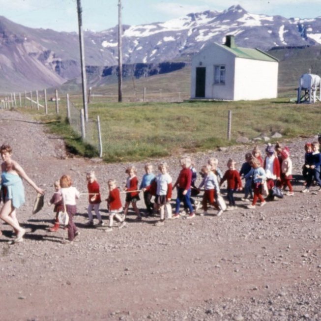Fóstrur og börn af róló í gönguferð í góðu veðri. Líklega er Dóra Haraldsdóttir fremst með börnin, en gaman væri að fá það staðfest og einnig fleiri nöfn.
