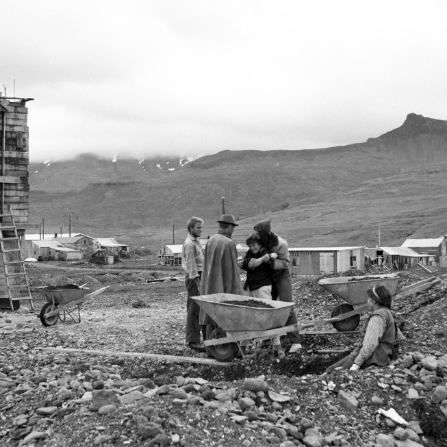 Þessi mynd er líklega frá árinu 1962? Verið er að steypa kirkjubygginguna sjálfa, lengst til vinstri á myndinni er byggingarmeistarinn Guðbjartur Jónsson, fyrir miðri mynd er hluti af vinnuflokknum sem vann við kirkjubygginguna og líklega er það Guðrún Agnarsdóttir þá læknanemi sem stendur lengst til hægri. Hús, skúrar og kofar sem eru í baksýn væri gaman að fá vitneskju um, en þekkja má Steinahlíð hús Steina á Arnarhóli og svo sést í þak nýja barnaskólans.