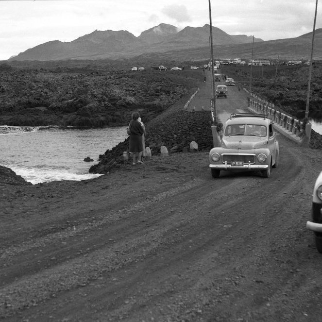 Líklega er þessi mynd frá 1961 þegar Mjósundabrúin var tekin í notkun, var hún mikil samgöngubót á sínum tíma. Á myndinni eru bifreiðarnar P-14 og P-515, það væri gaman að fá að vita meira um þá bíla og hverjir áttu bílanna og hvaða andlit má greina á myndinni?