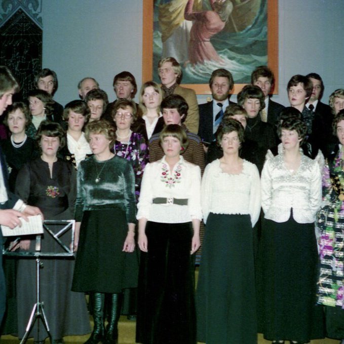 Á þessari mynd er Bjarki Sveinbjörnsson organisti, kórstjórnandi og skólastjóri tónlistaskólans að stjórna tónleikum. Í hvaða tilefni eru tónleikarnir og hvað kallaðist kórinn? Kórfélagar talið aftast frá vinstri: Sr. Jón Þorsteinsson, Guðmundur Runólfsson, Grímur Haraldsson, Ásmundur Karlsson, Halldór Hringsson, Tryggvi Gunnarsson, Guðni Gústafsson og Þórólfur Guðjónsson. Mið röðin, Ásdís Valdimarsdóttir, Elísabet Árnadóttir, Salbjörg Nóadóttir, Jensína Guðmundsdóttir, Aðalheiður Magnúsdóttir, Sunna Njálsdóttir, Edda Svava Kristjánsdóttir, Jóhanna Steinþóra Gústavsdóttir, Svava Axelsdóttir, Þórunn Björg Sigurðardóttir og Sigurrjós Árnadóttir. Fremsta röðin, Kristín Nóadóttir, Guðný Ingibjörg Hjartardóttir, Guðbjörg Hringsdóttir, Selma Friðfinnsdóttir, Kristín Friðfinnsdóttir og Elín Dagmar Valdimarsdóttir. Það má endilega leiðrétta ef rangt er farið með nöfnin og einnig eru tvær konur í þjóðbúning í miðröðinni sem ekki sjást en væri gaman að fá nöfn þeirra.