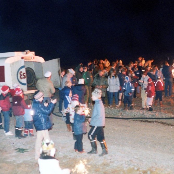 Á þessari mynd sjáum við að Ragnar Kristjánsson (Raggi í Sjoppunni) er mættur með olíubílinn svo að hægt sé að fíra upp í brennunni, börn og fullorðnir eru síðan með stjörnuljós og flugelda og yrði það sennilega stoppað snarlega í dag að vera með allan þennan eld rétt við brennu. Spurningin er hvaða ár er þetta og hvar er brennan þetta árið?