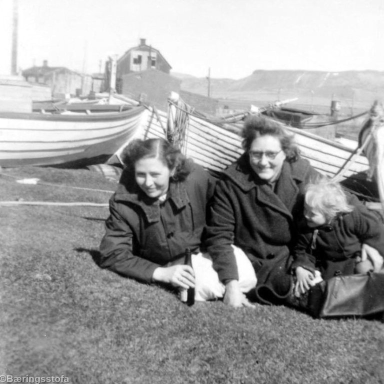 Þessi mynd sýnir ungar konur og litla stúlku sitja saman rétt hjá Neshúsunum þar sem trillurnar voru dregnar upp fyrir fjöruborðið og geymdar þar í skjóli. Talið frá vinstri, Ragnheiður Skarphéðinsdóttir, Áslaug Pétursdóttir og líklega Jóhanna Kristín Kristjánsdóttir dóttir Ásu.