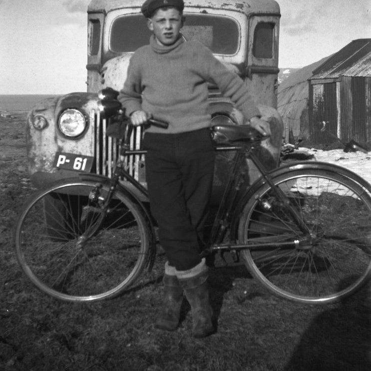 Þessa skemmtilegu mynd hefur Bæring tekið um það leiti sem fólkið er að flytjast frá sveitinni og setjast að í þorpinu Grafarnesi. Ungi maðurinn sem styður sig við reiðhjólið Bærings er Þorvaldur Elbergsson.  Í baksýn er gamall og lúin bíll P-61 sem gaman væri að fá nánari deili á.