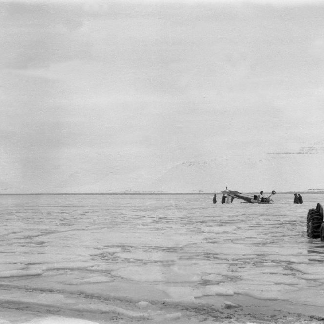 Þarna hefur flugvél nauðlent og síðan hvolft á firðinum, fróðlegt væri að fá fleirri upplýsingar um atburðin. Það sem einnig vekur athygli er hvað grunt sýnist vera þarna miðað við traktorinn og mennina sem standa við flugvélina.