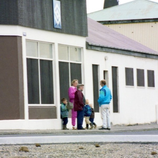 Skemmtileg mynd sem Bæring hefur tekið af daglega lífinu í Grundarfirði. Oft var spjallað í og við Kaupfélagið. Þarna hittast þau á förnum vegi þau Jóhanna Magnúsdóttir (Nóa), Pétur Konráðsson (Pétur Konn) og Níels Friðfinnsson (Nilli Finna) sem líklega er að tékka á kostinum sínum sem keyrður var niður á bryggju í kaupfélags bílnum sem stendur þarna lengst til hægri á myndinni. Börnin sem eru á myndinni eru þeir bræður Hallgrímur Hallgrímsson (Halli) og Tónas Logi Hallgrímsson (Tommi) sem eru þarna með Nóu ömmu sinni og vini sínum Víking Guðjónssyni. Gaman væri að fá nafn ungu konunnar með litlu stelpuna í kerru (litla stelpan gæri verið fædd 1987 eða 1988).