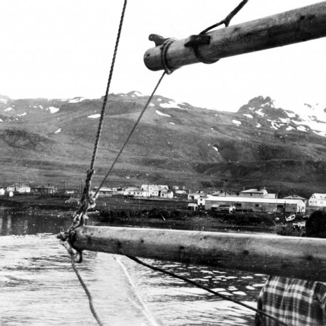 Bátur siglir inn Grundarfjörð og er að koma upp að bryggjunni. Gaman væri að vita meira um þessa skemmtilegu mynd sem er tekin sjötta áratugnum. Getur verið að þetta sé Grundfirðingur ll ? Getur verið að þeir séu að koma af síld frá Siglufirði? Og getur verið að einhver þekki manninn á myndinni sem horfir til lands?                              Þéttbýlið í Grundarfirði hefur tekið miklum breytingum á þessum áratugum sem liðnir eru frá því að myndin var tekin. Þarna má sjá húsin við Grundargötu frá númer 8 – 24. Bjarg, Ásgarð, Vinaminni, Götuhús, Björnshús, Bifröst, Búðir, Snarræði, Vík og Björgvinshús. Við sjávarsíðuna eru svo Lengja og Grund (Fiskverkun Soffaníasar).