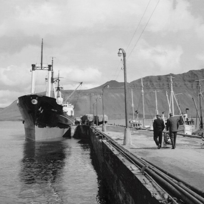Alltaf nóg að gera á höfninni. Þarna er líklega í gangi útskipun á saltfisk um borð í Fjallfoss. Það var ekki algeng sjón að sjá karlmenn með barnavagna úti að spássera en þegar það gerðist þá var farið niður á bryggju og aðeins á sunnudögum. Ágiskun er að þarna sé Aðalsteinn Friðfinnsson á ferð með dætur sínar Önnu Jonny í kerrunni og Olga Sædís með dúkkuvagninn (dúkkuvagninn þekkist) og er þá myndin tekin vorið 1965. Spurning hvort hinn maðurinn sé Guðni frá Berserkseyri, endilega komið með ábendingar.