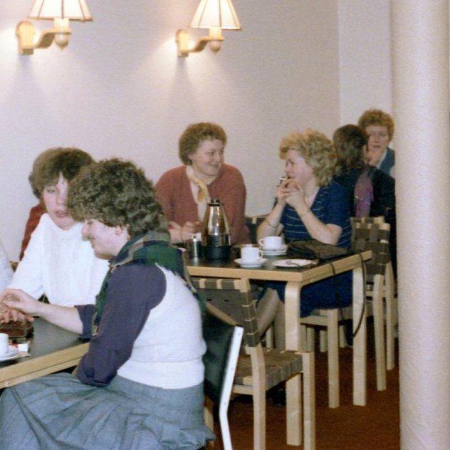 Kvenfélagsfundur í Safnaðarheimilinu, spjallað yfir kaffibolla. Við fremsta borðið eru þær Ólafía Hjálmarsdóttir, Bryndís Theódórsdóttir og Sigrún Edda Hringsdóttir. Við næsta borð sitja þær Hulda Valdimarsdóttir og Elsa Fanney Pétursdóttir og við þriðja borðið sitja þær Marta Böðvarsdóttir (Maddý á Akurtröðum), Inga Sveinsdóttir og Margrét Hallsdóttir (Maddý á Naustum) og það er spurning hvort það sé Ásdís Garðarsdóttir sem snýr baki í myndavélina?