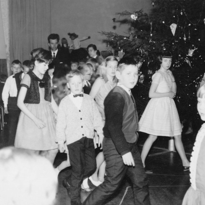 Jólaball í samkomuhúsinu, prúðbúin börn að ganga í kringum jólatréð með séra Magnúsi Guðmundssyni. Gátan er: hvað heita börnin og konan sem situr upp við vegginn? Við eigum mörg hver minningar til margra ára frá jólaböllum Kvenfélagsins Gleym mér ei. Risastórt jólatré, tónlist, jólasveinar, fullorðna fólkið að ganga með í kringum jólatréð og sitja við vegginn þar sem gott var að fylgjast með og allir í sparifötunum sínum.